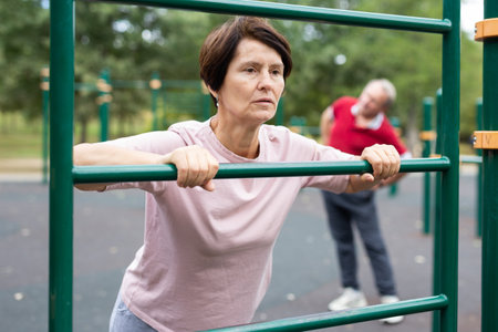 Elderly woman doing exercises on sports bars at outdoor sports groundの写真素材