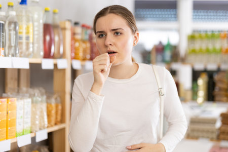 Woman coughing standing in supermarketの写真素材