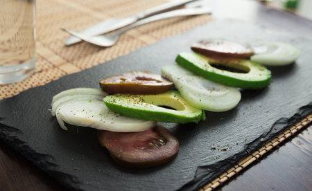 Chopped vegetables black tomatoes, avocado and onions against black stone boardの写真素材