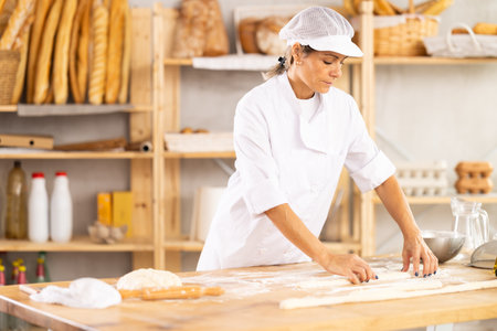 Female baker rolls dough into long sausages to be cut into pieces for baking bunsの写真素材