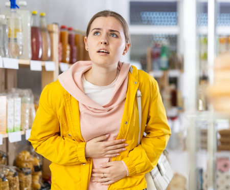 Young woman with stomach pain in grocery storeの写真素材