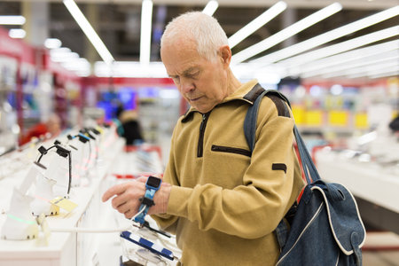 Elderly man examines smart watch in showroom of electronics storeの写真素材