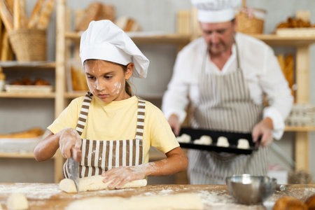 Little girl, baker assistant, cutting raw dough with knifeの写真素材