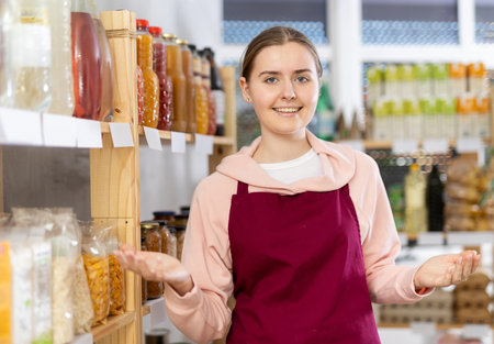 Portrait of female seller in an apron behind the counter of grocery storeの写真素材