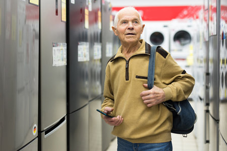 Elderly man choosing refrigerator in showroom of electrical appliance storeの写真素材