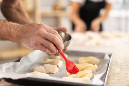 Close up of baker hands brushing uncooked dough pieces on baking sheet with oil before baking in ovenの写真素材