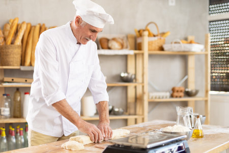 Elderly man baker rolls out doughの写真素材