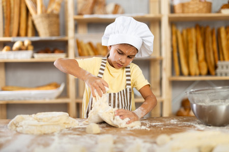 Little girl baker learning to knead dough in bakery kitchenの写真素材