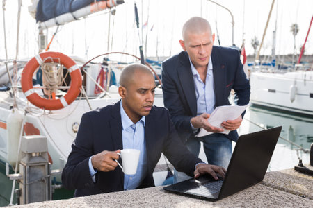 Men in suits verifying documentation on a laptop in the seaportの写真素材