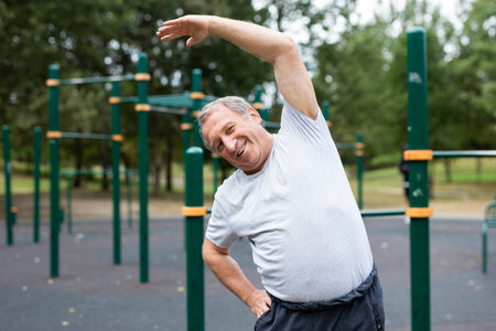 Elderly man doing gymnastics on an outdoor sports groundの写真素材