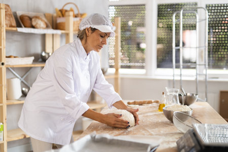 Working in bakery - woman kneads raw dough to make baguettes or croissantsの写真素材
