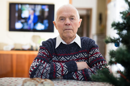 Bored elderly man sitting alone at table with small Christmas tree.の写真素材