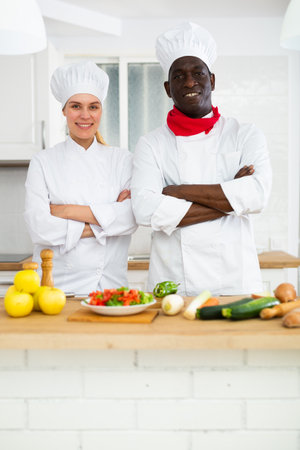 Two smiling confident personal chefs in white uniforms standing in private kitchenの写真素材