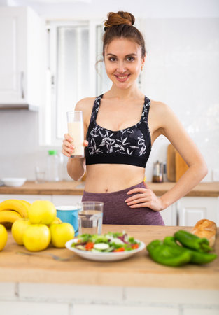 Positive young woman drinking dairy product at homeの写真素材