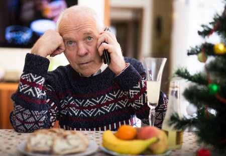 Upset older man talking on phone at table during New Year celebrationの写真素材