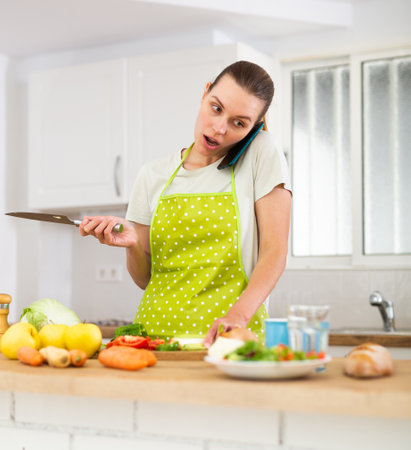 Woman talking on mobile phone while cooking dinner in kitchenの写真素材