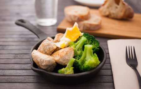Ppieces of fried chicken breast with boiled broccoli and poached egg in cast iron portioned skilletの写真素材