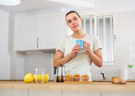 Dreamy young woman standing in home kitchen with cup of coffeeの写真素材