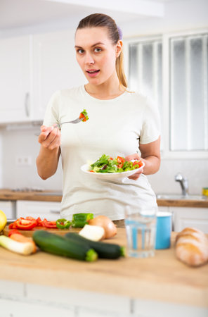 Positive housewife eating homemade salad in kitchenの写真素材