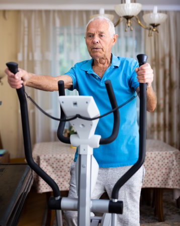 Fit senior man at home doing cardio work out on an elliptical machineの写真素材