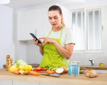 Young housewife using phone to find recipe while cooking dinnerの写真素材