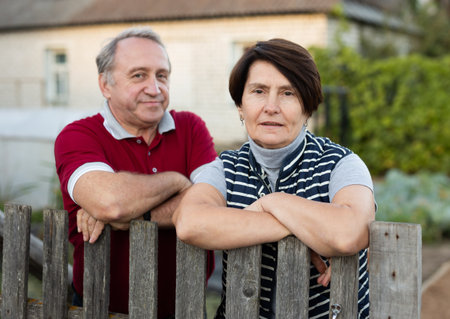 Positive mature man and woman standing near fence in gardenの写真素材