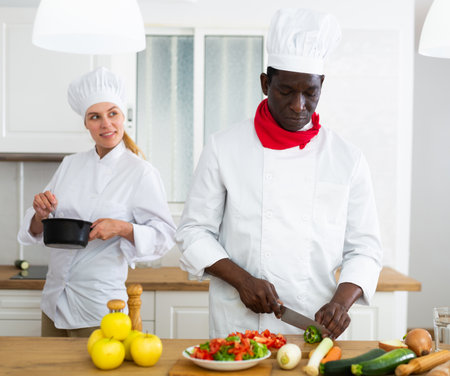 Professional chef in white uniform working with female assistant in private kitchenの写真素材