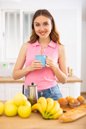 Smiling brown-haired woman enjoying cup of coffee in home kitchenの写真素材
