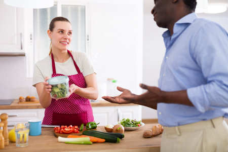Wife in apron handing food container to husband in kitchenの写真素材