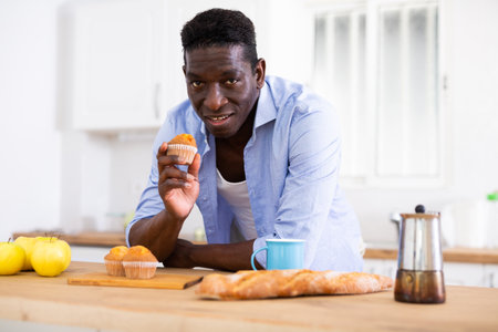 man eating sweet cupcakes in kitchen during breakfastの写真素材