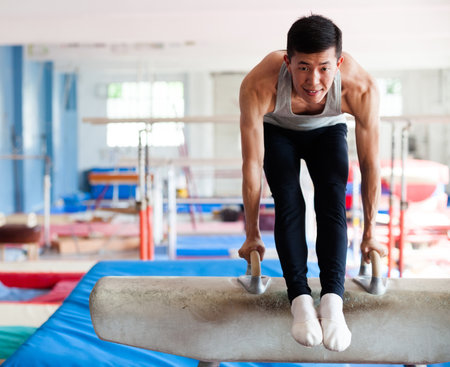 Male athlete doing complicated exciting trick on pommel horse in professional gymの写真素材