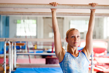 Woman gymnast performs complex acrobatic exercise on parallel bars in gymの写真素材