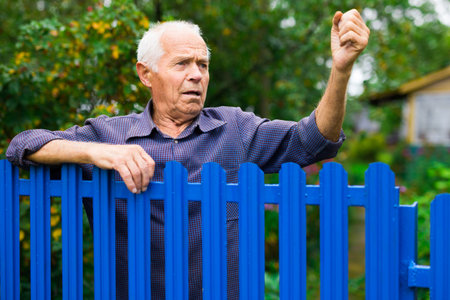 Old man showing fist outdoors beside fenceの写真素材
