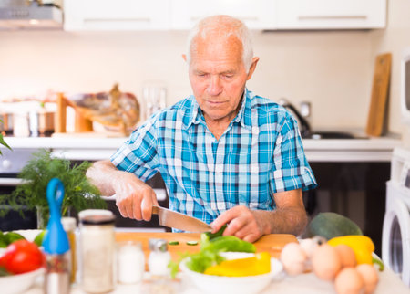 senor man preparing fresh vegetable salad at home in the kitchenの写真素材