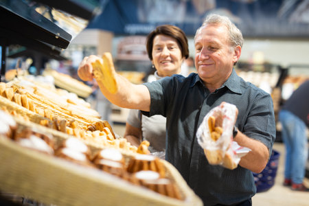 Man and woman choose hot fresh buns and bread on supermarket showcaseの写真素材