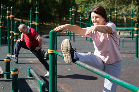 Positive elderly woman doing leg stretching on outdoor sports ground