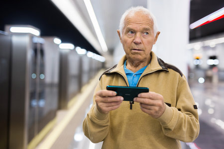 Senior man with smartphone waiting in subway stationの写真素材