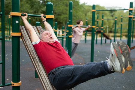 elderly man doing exercises on a horizontal bar at an outdoor sports ground