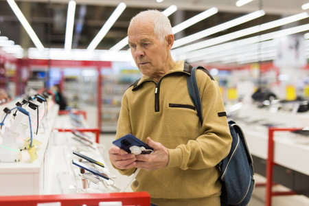 elderly man examines tablet computer in showroom of electronics storeの写真素材