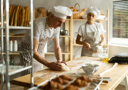Man and woman, experienced bakers, prepare dough for baguettes and croissants together in private...