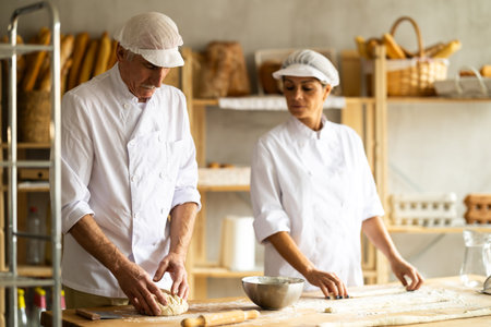 Elderly male chef and female skillfully kneads dough to bake delicious bread and croissantsの写真素材