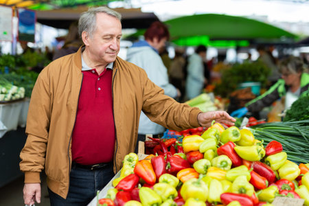 Casual senior male customer choosing organic vegetables while walking at local marketの写真素材