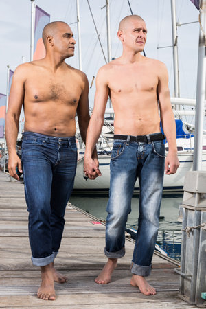 romantic couple of young men walking together on the pavement in the portの写真素材