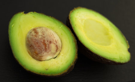 Delicious ripe avocado cut in half with pit on black stone board