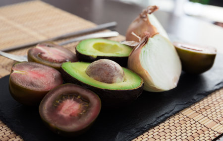 vegetables black tomatoes, avocado and onions on black stone board