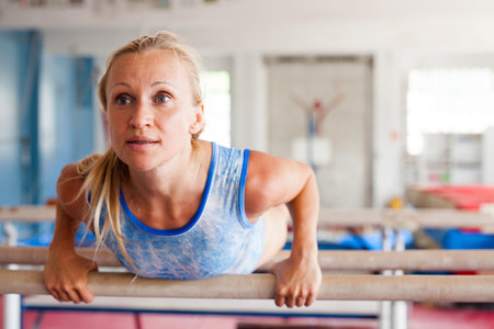 Woman gymnast performs complex acrobatic exercise on parallel bars in gym