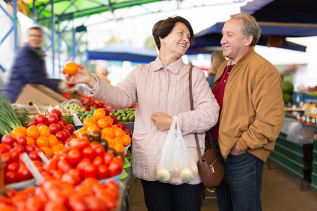 elderly man and woman buy vegetables at an open marketの写真素材