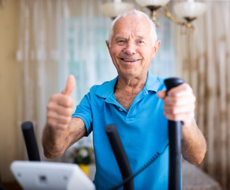 Senior man with elliptical trainer at homeの写真素材