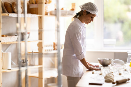 Female baker rolls dough into long sausages to be cut into pieces for baking bunsの写真素材