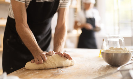Closeup of baker hands kneading raw dough on kitchen table in bakery